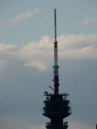 Low angle view of communications tower by building against sky