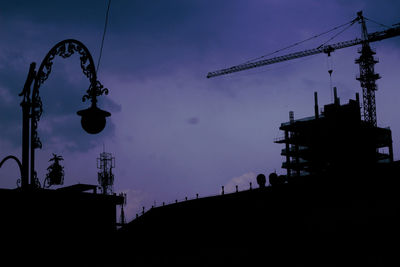 Low angle view of silhouette cranes against sky at dusk