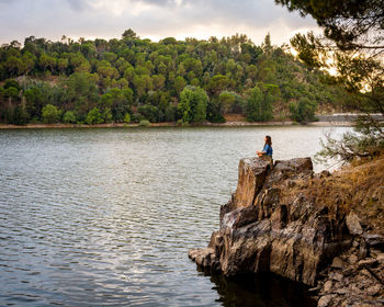 Side view of woman meditating while sitting on rock by river