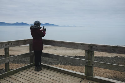 Man standing on mobile phone by sea against sky