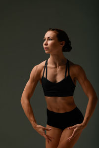 Young woman looking away while standing against black background