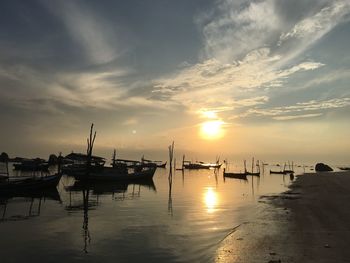 Silhouette boats moored at harbor against sky during sunset