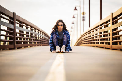 Full length portrait of young woman sitting on railing