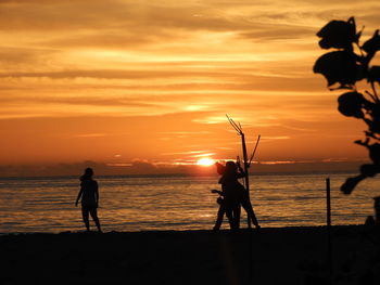 Silhouette people on beach against sky during sunset