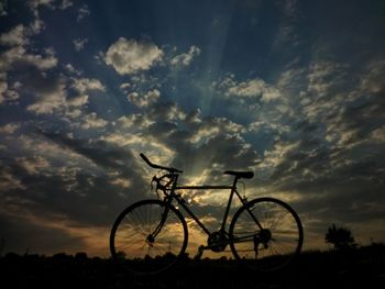 Silhouette bicycle on field against sky