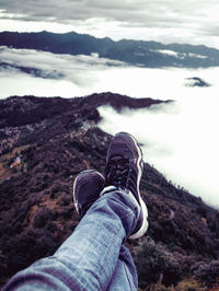 Low section of person on cliff amidst cloud