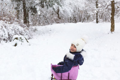 A little girl in warm clothes is sitting on a sleigh. winter forest, walk