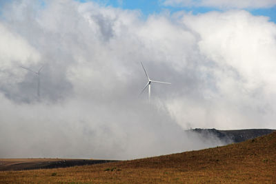 Low angle view of wind turbines on field