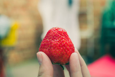 Close-up of hand holding strawberry against blurred background