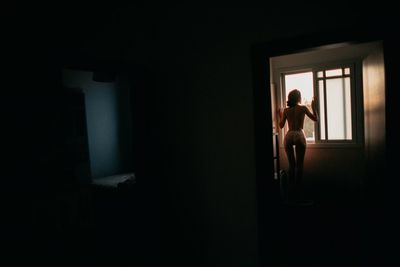 Rear view of topless woman looking through window