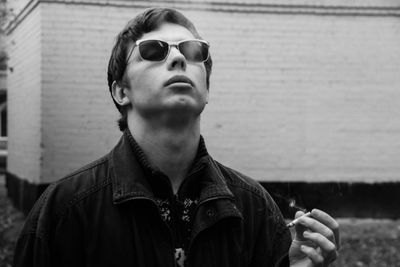 Man in sunglasses smoking cigarette against wall