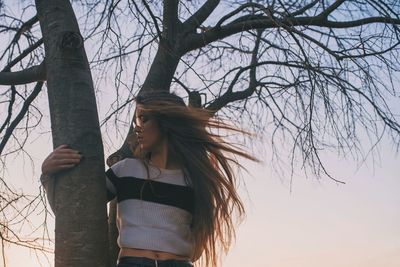 Woman standing by tree trunk against sky