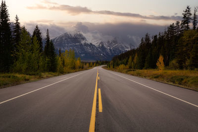 Empty road along trees and mountains against sky