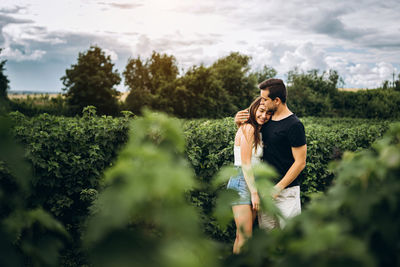 Full length of couple standing by plants against sky