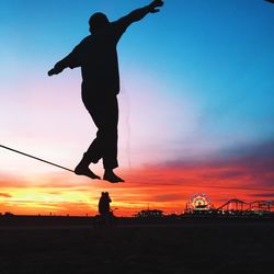 Silhouette man performing slackline at beach against sky during sunset