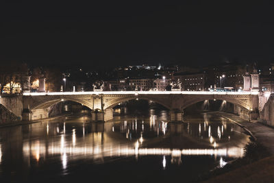 Illuminated bridge over river in city against sky at night