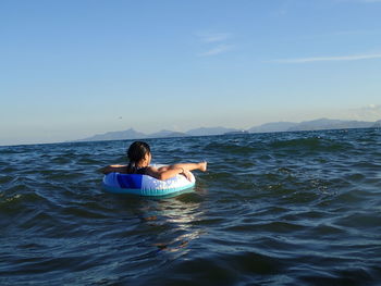 Woman sitting on inflatable ring in sea against clear sky