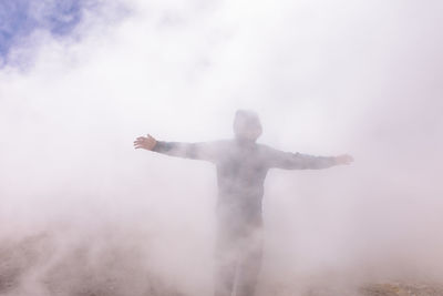 Man with arms outstretched standing in fog