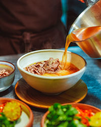 Unknown chef pouring broth into a chicken soup with meat and vegetable. pho bo