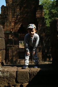 Full length of boy standing against stone wall