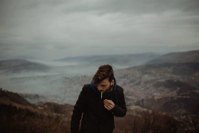 Man smoking cigarette while standing on mountain against sky