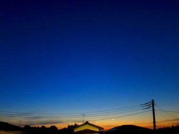 Silhouette electricity pylons against clear blue sky at sunset