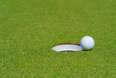 Golf ball on lip of cup at golf court.