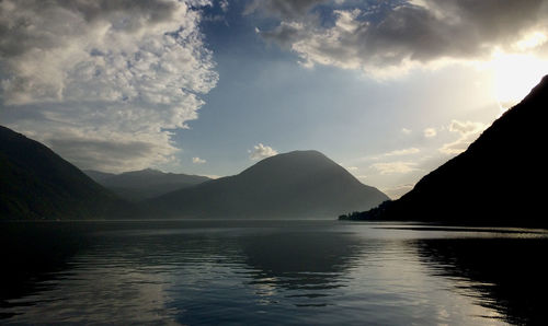 Scenic view of lake by silhouette mountains against sky