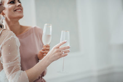 Midsection of bridesmaid and bride holding champagne flute