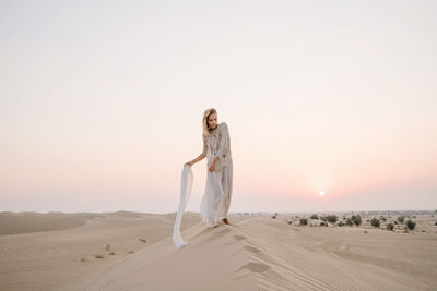 Woman standing in desert against sky during sunset