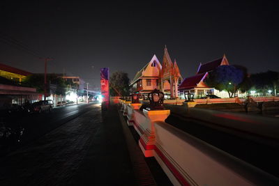 Illuminated buildings by street against sky at night