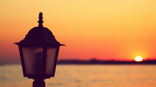 Silhouette built structure against sea during sunset