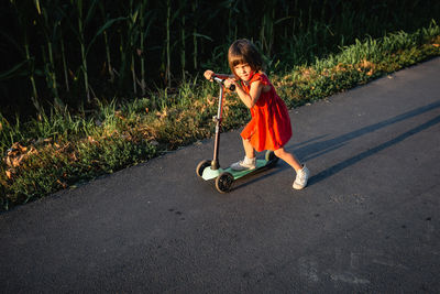 Girl in red dress riding green scooter on a country road against the sun