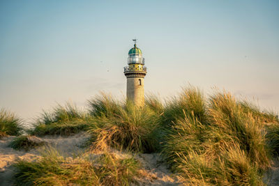 Lighthouse in sand dunes amidst buildings against sky