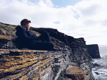 Man sitting on rock against sky