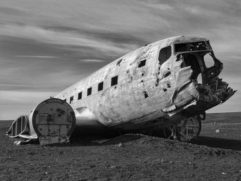 Abandoned airplane on sand at beach against sky