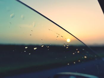 Close-up of wet glass window against sky during sunset