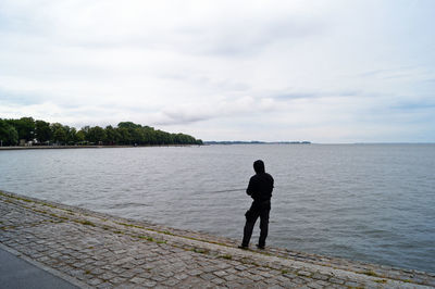 Rear view of man standing by river against sky
