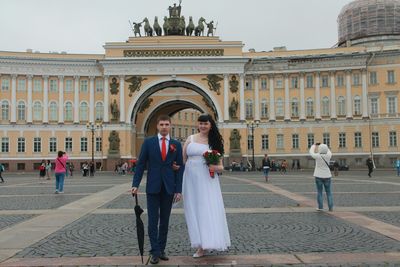Portrait of newlywed couple standing at palace square against arka glavnogo shtaba