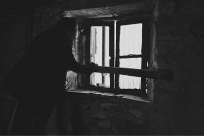 Side view of woman standing against window in abandoned building