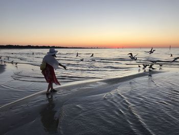 Rear view of woman at beach against sky during sunset