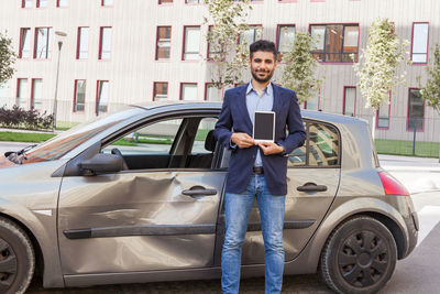 Full length portrait of man standing against car