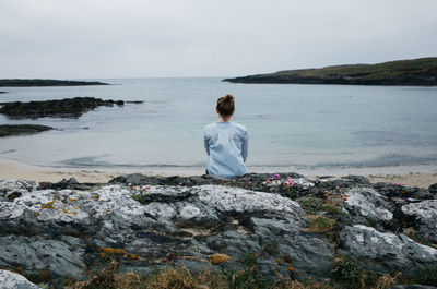 Rear view of woman sitting on rock against sea