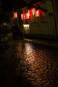 Illuminated building by wet street at night