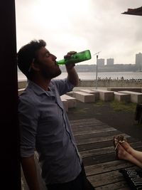 Man drinking water in city against sky