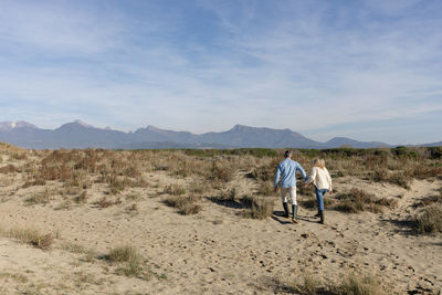 Couple walking together amidst plants on sand at dunes