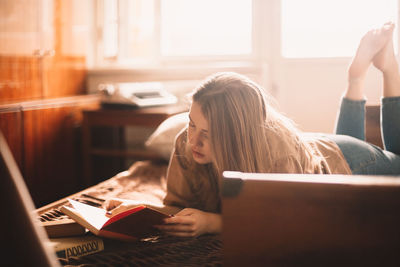 Young woman reading book while lying on bed at home