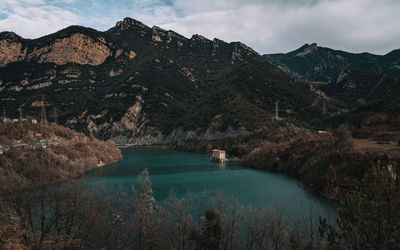 Scenic view of lonely house by lake and mountains against sky