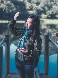 Young woman shielding eyes while standing by railing and lake