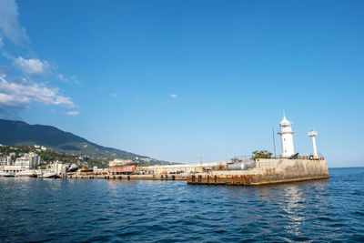 Lighthouse amidst sea and buildings against sky